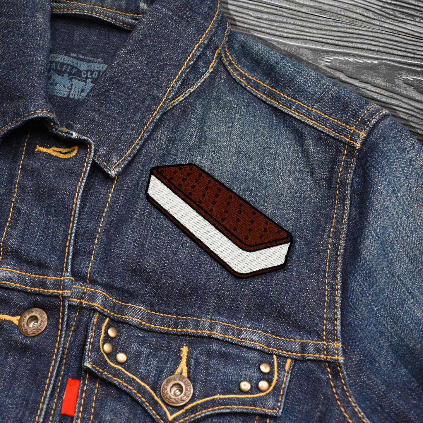 Denim jacket with a patch of an ice cream sandwich on a wooden surface