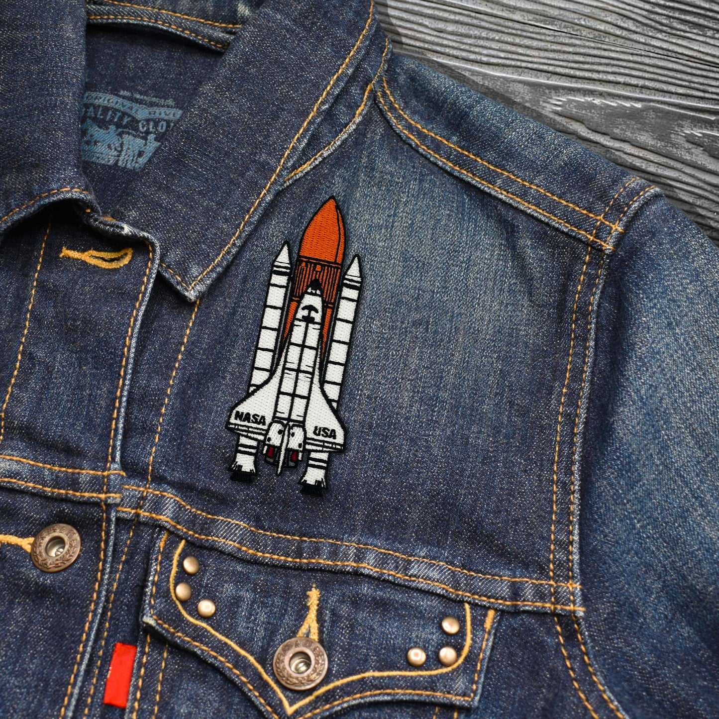 Denim jacket with a NASA space shuttle patch on a wooden surface