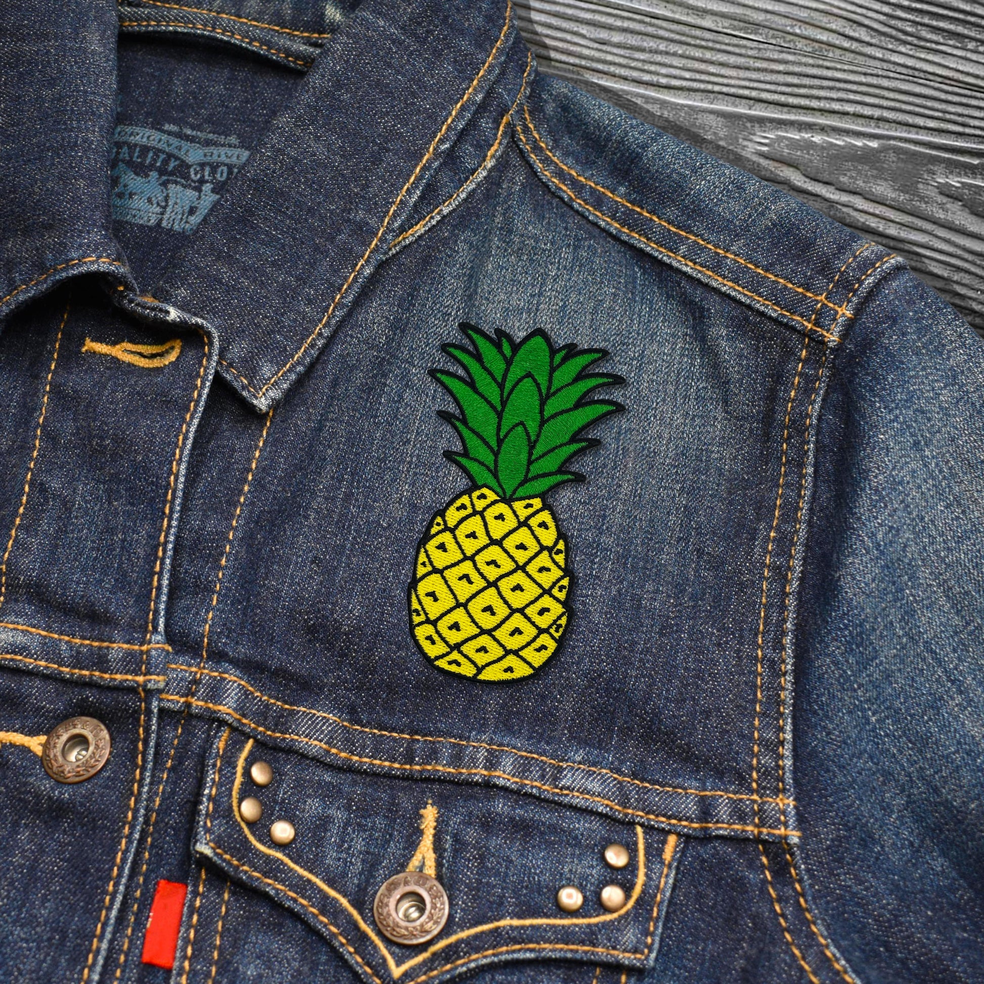 Denim jacket with a pineapple patch on a wooden surface