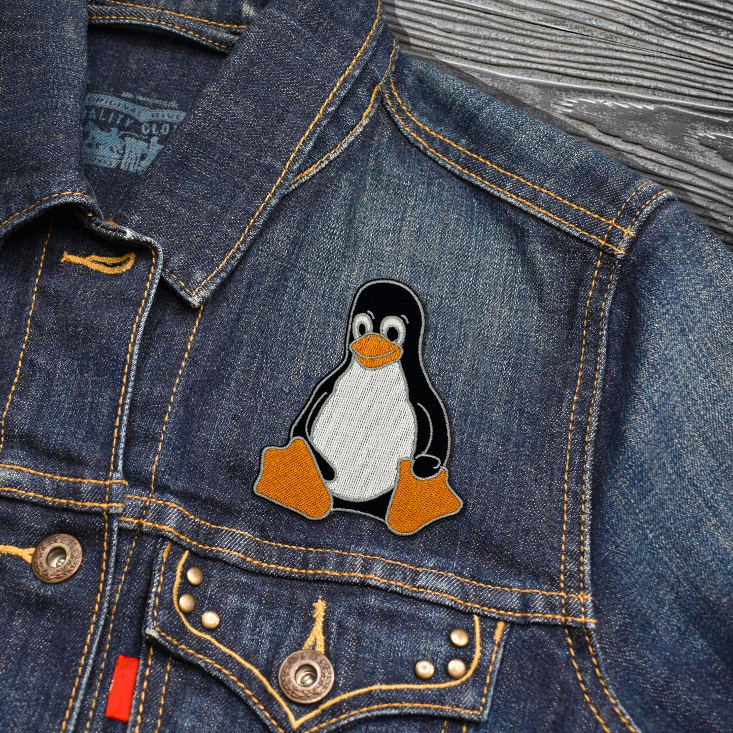 Denim jacket with a Tux the Linux Penguin patch on a wooden surface