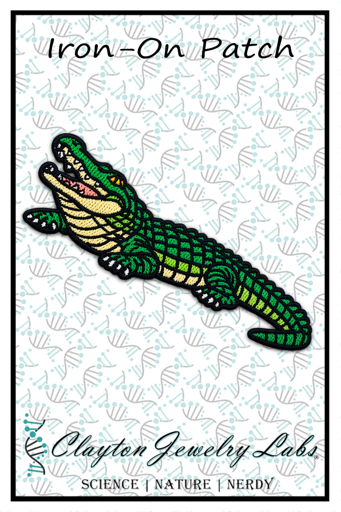 An embroidered iron-on patch of a cartoon alligator with an open mouth, featuring green scales, a cream underbelly, and black outlines, displayed on a white patterned background with the text 'Iron-On Patch' and 'Clayton Jewelry Labs'.