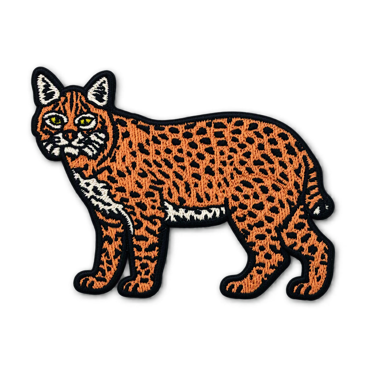 An embroidered patch of a wildcat or lynx in profile, featuring an orange and black spotted pattern with white accents on its chest, paws, and ears, and yellow eyes, all outlined in black thread on a white background.