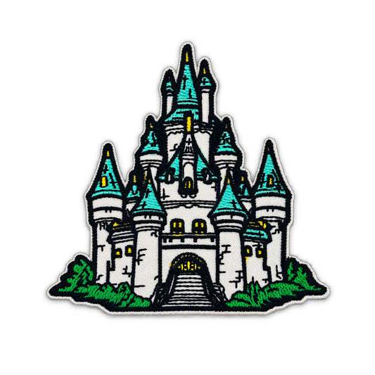 An embroidered patch featuring a stylized white castle with turquoise-blue spires, green grass, and yellow window lights on a white background.