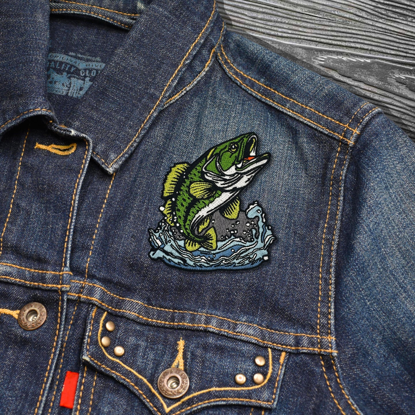Denim jacket with a fish patch on a wooden surface
