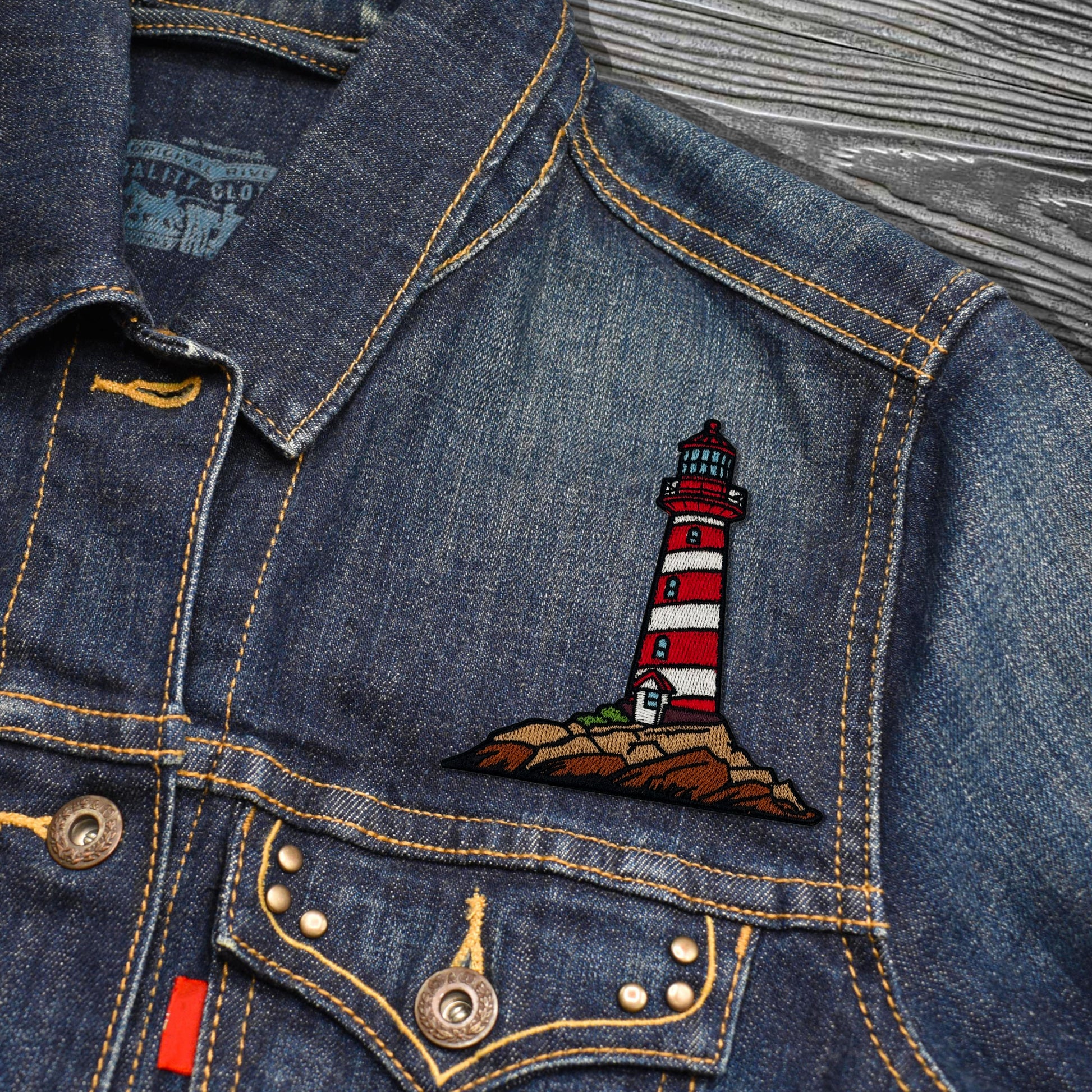 Denim jacket with a lighthouse patch on a textured surface