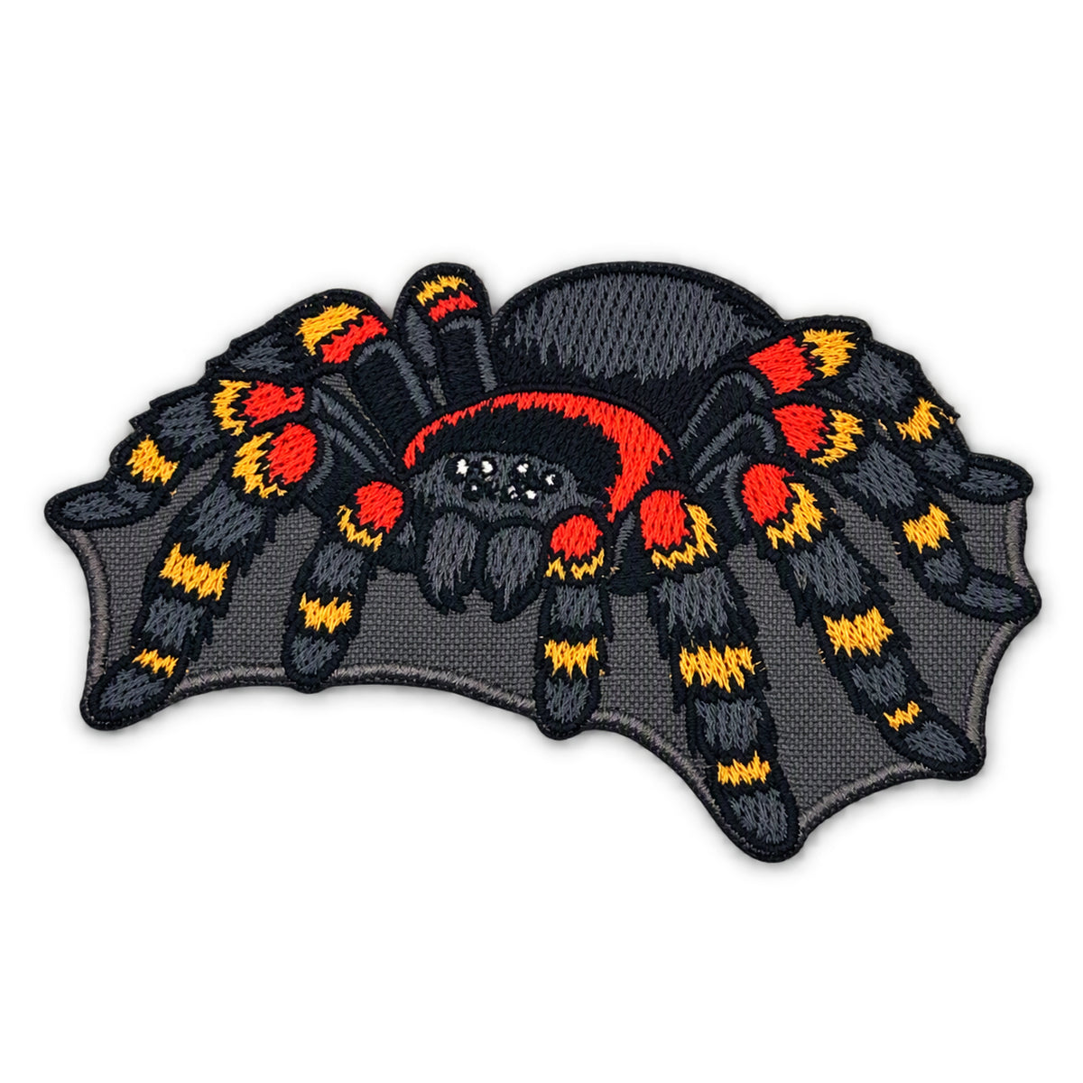 An embroidered patch of a tarantula spider on a dark gray bat-wing-shaped background, featuring black, red, and yellow color details, shown on a plain white background.