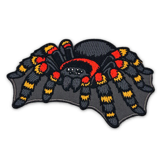 An embroidered patch of a tarantula spider on a dark gray bat-wing-shaped background, featuring black, red, and yellow color details, shown on a plain white background.