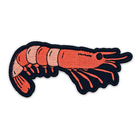 An embroidered iron-on patch of a shrimp, featuring a bright orange-red body with pinkish-beige segmented accents and a black embroidered border.