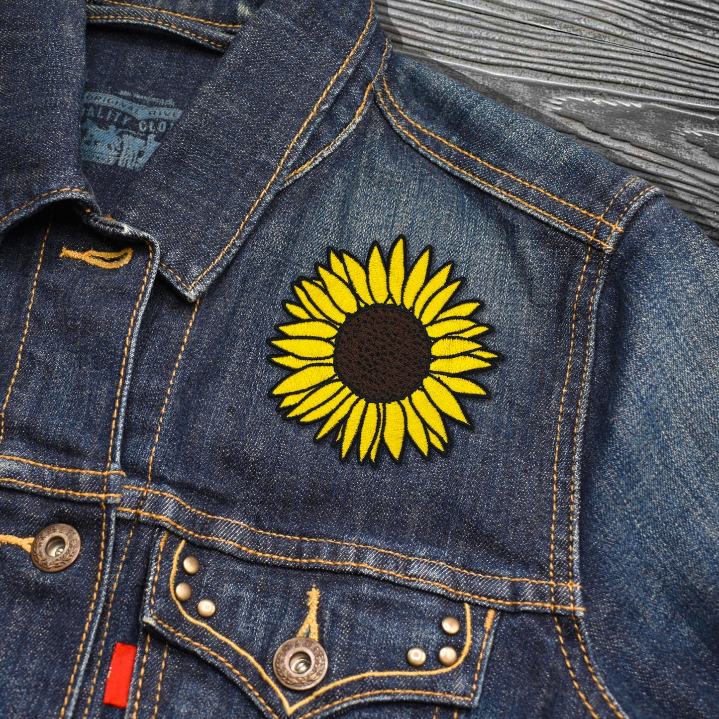 Denim jacket with a yellow sunflower patch on a wooden surface