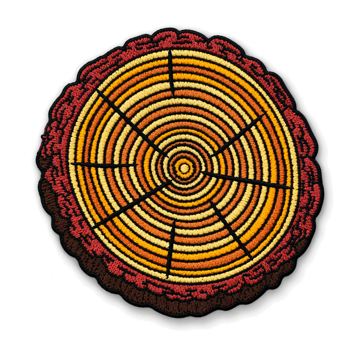 A circular embroidered patch depicting a tree trunk cross-section with concentric rings in shades of orange, yellow, brown, and red, finished with a black scalloped border on a white background.